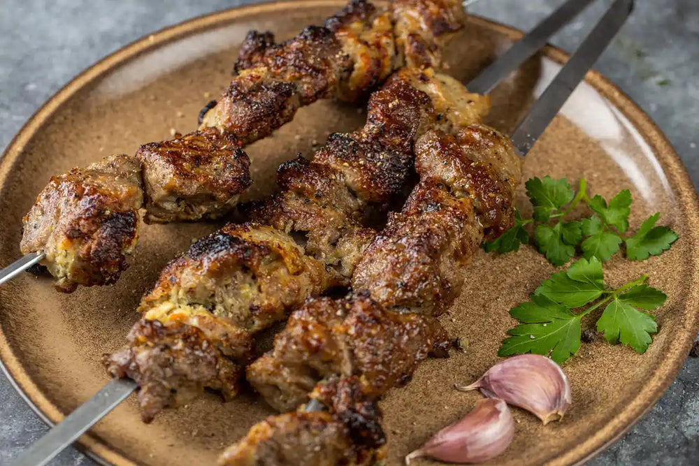 Nahaufnahme Schweine Schaschlik Knoblauch Pfeffer auf Spießen serviert auf Teller mit Knoblauch und Petersilie