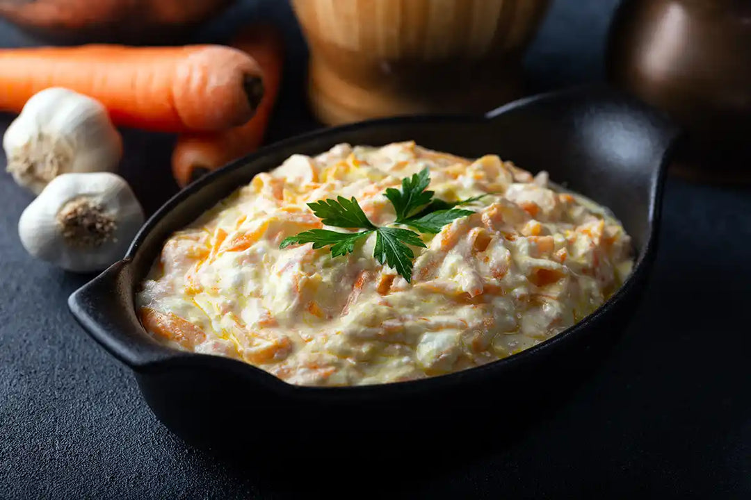 Leckerer Karotten Käse Salat serviert in einer kleinen Schale, garniert mit Petersilie und dekoriert mit Knoblauch, Karotten und Gewürzmühlen. Serviervorschlag.