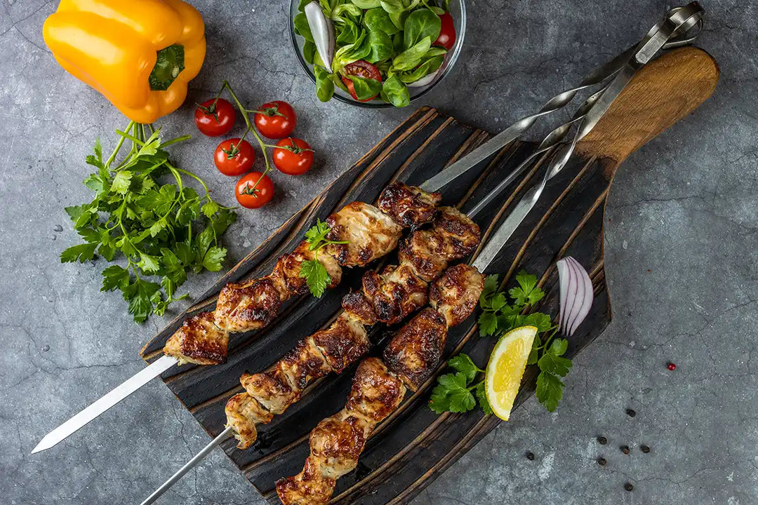 Pute Schaschlik Original auf einem Holzbrett angerichtet, garniert mit Zitrone, Petersilie und Zwiebel. Dekoriert auf einer Arbeitsplatte mit Cherrytomaten, Salat, Paprika und Gewürzmühlen aus Holz. Serviervorschlag.