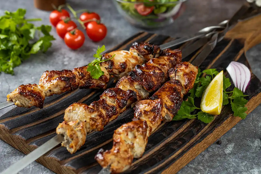 Pute Schaschlik Original auf einem Holzbrett platziert, garniert mit Zitrone, Petersilie und Zwiebel. Dekoriert auf einer Arbeitsplatte mit Cherrytomaten, Salat, Paprika und Gewürzmühlen aus Holz. Serviervorschlag.