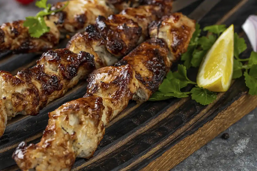 Nahaufnahme von gegrilltem Schaschlik aus Putenfleisch. Angerichtet auf einem Holzbrett mit Petersilie, Zitrone und roter Zwiebel. Serviervorschlag.