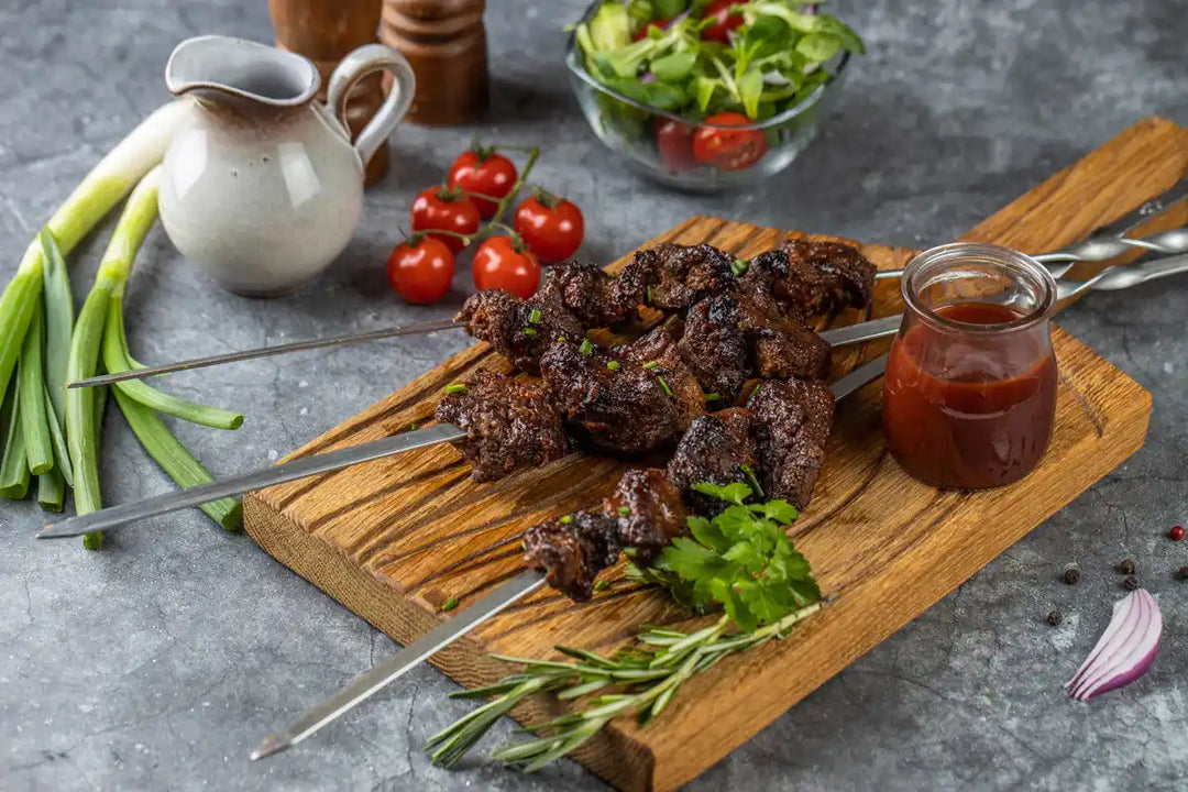 Rinder Schaschlik Barbecue auf Spießen serviert auf Holzbrett mit Petersilie und Barbecue Sauce