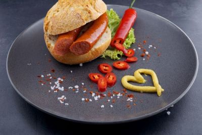 Feuerwurst in Brötchen serviert auf Teller mit Senf und Peperoni
