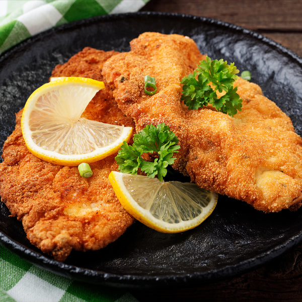 Hähnchenschnitzel gebraten serviert auf Teller mit Zitrone und Petersilie 