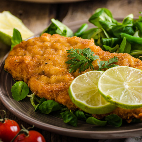 Schweineschnitzel gebraten auf Teller mit Salat und Zitrone serviert