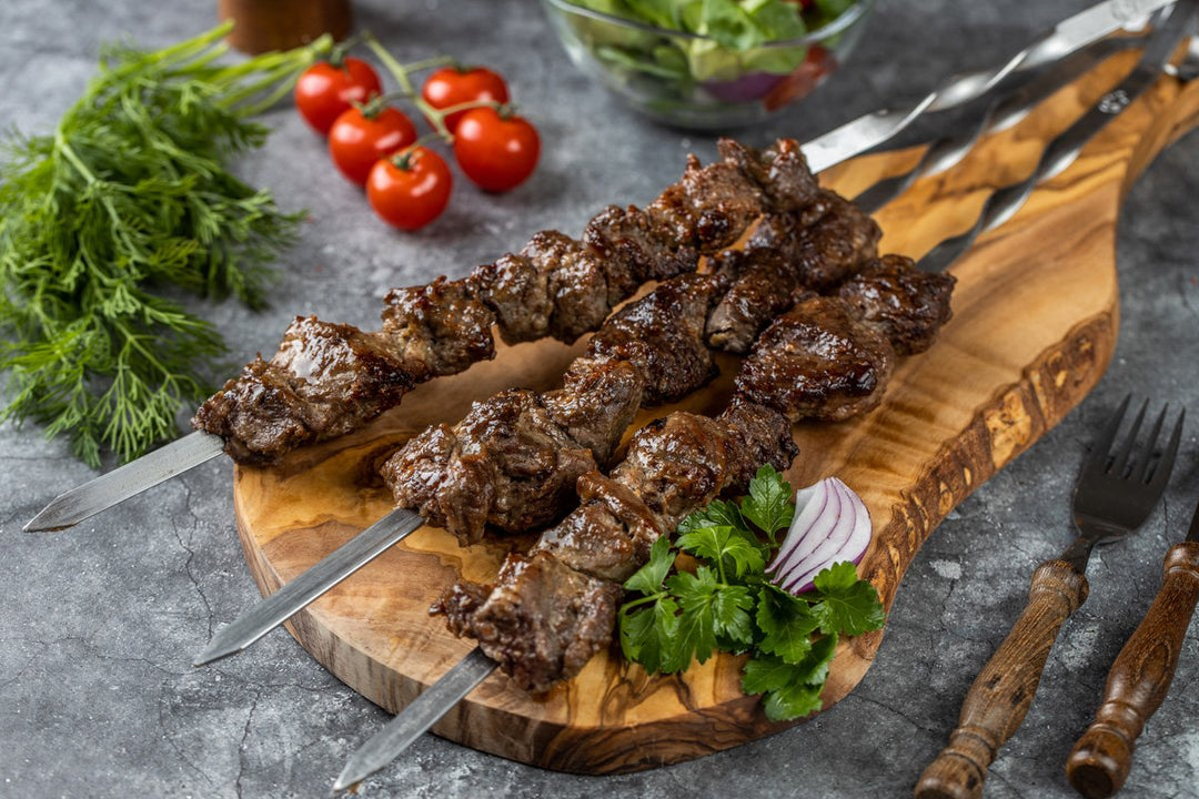 fertig gegrilltes Lamm-Schaschlik Original liegend auf einem Holzbrett. Mit roter Zwiebel und Petersilie dekoriert