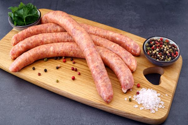 Hausmacher grobe Bratwurst serviert auf Holzbrett mit Gewürzen und Petersilie