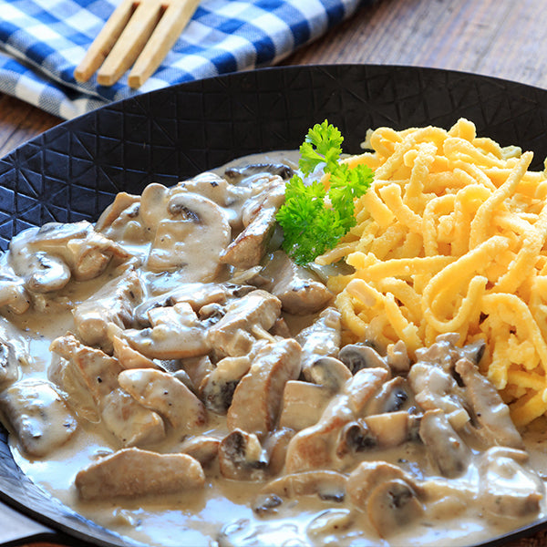 Schweinegeschnetzeltes in Champignon Rahmsauce mit Spätzle serviert in einer Pfanne